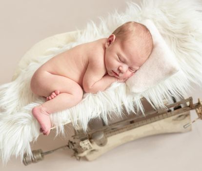 Cute newborn baby on a retro weight scale, isolated on beige background