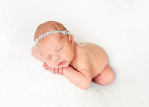 Naked innocent baby laying on fabric bedcover with headband