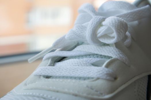 White athletic lace-up sneakers. White laces are tied close-up. Blurred background. Sports concept. Metal rivet for shoes as a detail or an element. Fashionable and stylish footwear