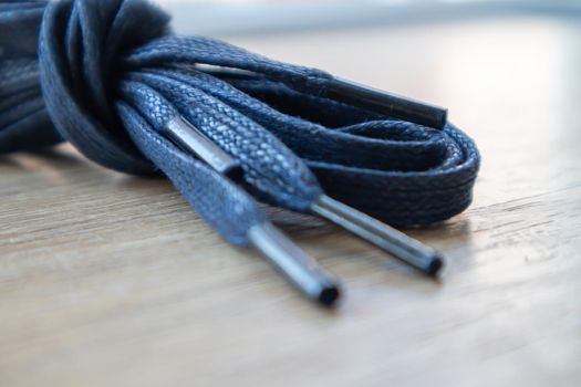 A subject shot of dark blue flat laces with thin tips for shoes rolled up and isolated on a wooden background. Stylish accessory