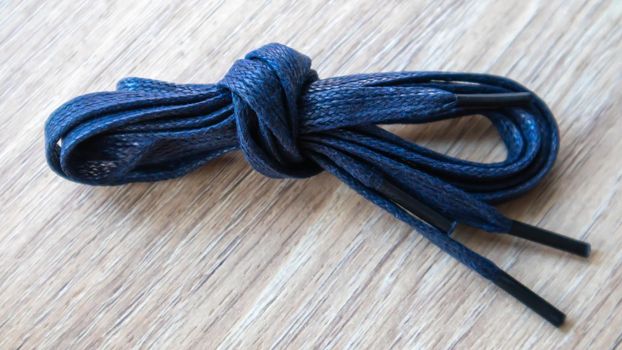 A subject shot of dark blue flat laces with thin tips for shoes rolled up and isolated on a wooden background. Stylish accessory
