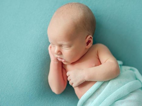 Little newborn wrapped in blue blanket resting in room