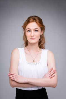 portrait vertical up to the waist young, beautiful business woman, student with lred, curly hair and freckles on gray background. SHe dressed in a white blouse with short sleeves about open shoulders.