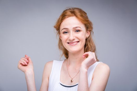 Closeup portrait young, beautiful business woman, student with lred, curly hair and freckles on face on gray background in the studio. Dressed in white blouse with short sleeves about open shoulders.