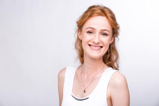 Portrait of a beautiful young female student with a smile in a white shirt of European, Caucasian nationality with long red hair and freckles on her face posing on a white background in the studio.