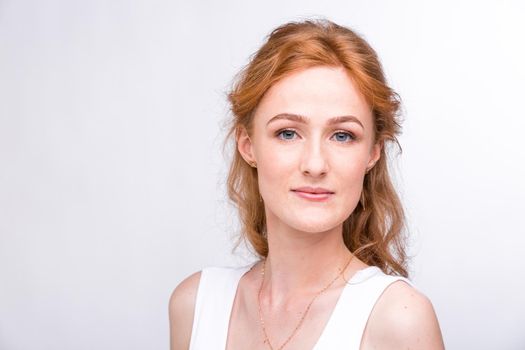 Portrait of a beautiful young woman of European, Caucasian nationality with long red hair and freckles on her face posing on a white background in the studio. Close-up student girl in a white blouse.