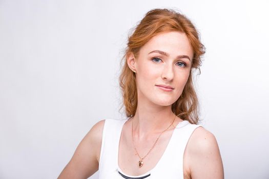 Portrait of a beautiful young woman of European, Caucasian nationality with long red hair and freckles on her face posing on a white background in the studio. Close-up student girl in a white blouse.