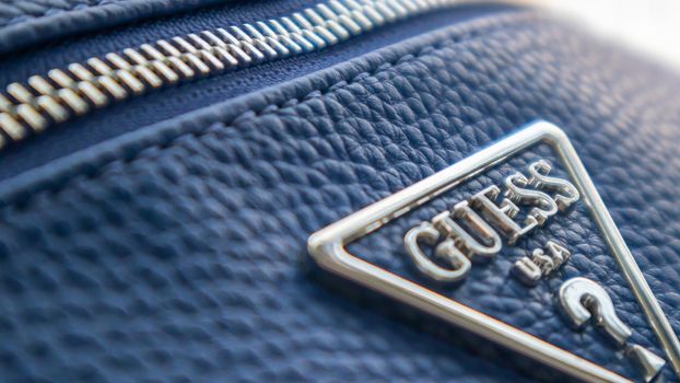 Blue Leather Shoulder Bag by GUESS. Triangular metal logo close-up. Ukraine, Kiev - June 17, 2021