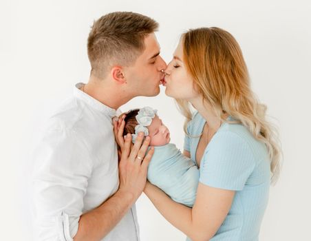 young beautiful parents are kissing and holding a newborn daughter. white background