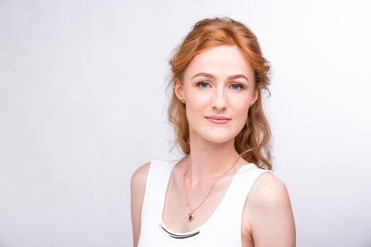 Portrait of a beautiful young woman of European, Caucasian nationality with long red hair and freckles on her face posing on a white background in the studio. Close-up student girl in a white blouse.