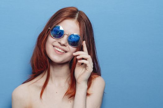 perky red-haired woman in blue glasses bare shoulders posing. High quality photo