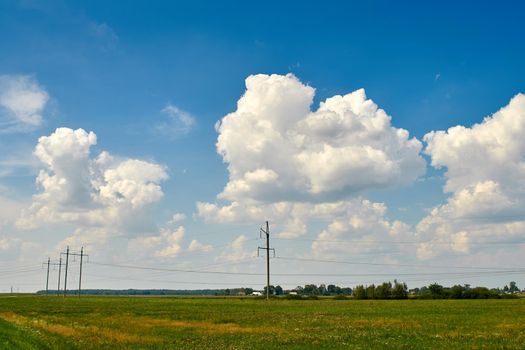 Huge white clouds in the sky over green fields, trees, forests. sunne day. Electric poles