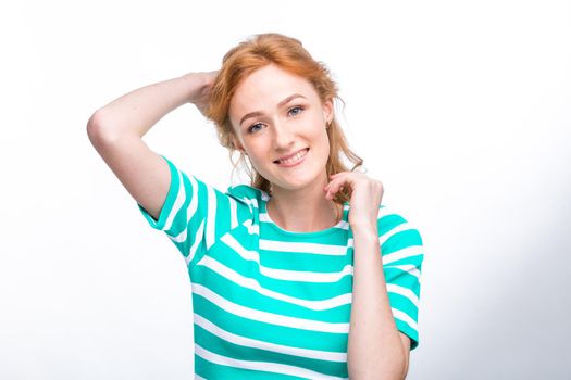 Close-up portrait of a young, beautiful woman with red curly hair in a summer dress with strips of blue in the studio on a gray background. Theme of summer vacation, tourism and summer clothes.