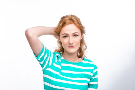 Close-up portrait of a young, beautiful woman with red curly hair in a summer dress with strips of blue in the studio on a gray background. Theme of summer vacation, tourism and summer clothes.