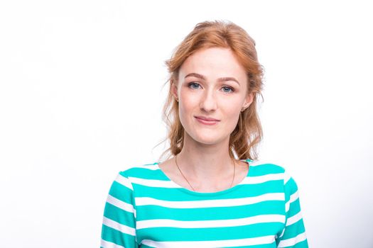 Close-up portrait of a young, beautiful woman with red curly hair in a summer dress with strips of blue in the studio on a gray background. Theme of summer vacation, tourism and summer clothes.