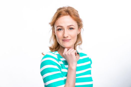 Close-up portrait of a young, beautiful woman with red curly hair in a summer dress with strips of blue in the studio on a gray background. Theme of summer vacation, tourism and summer clothes.