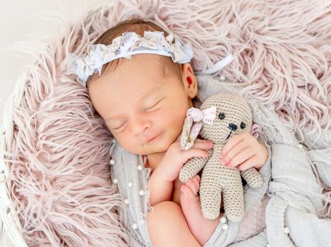 smiling newborn baby girl sleeping sweetly in the basket with a small toy