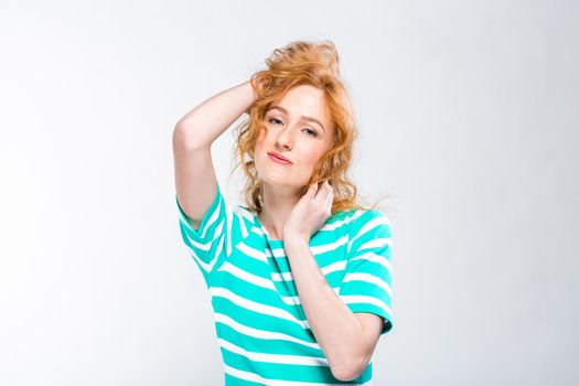 Close-up portrait of a young, beautiful woman with red curly hair in a summer dress with strips of blue in the studio on a gray background. Theme of summer vacation, tourism and summer clothes.