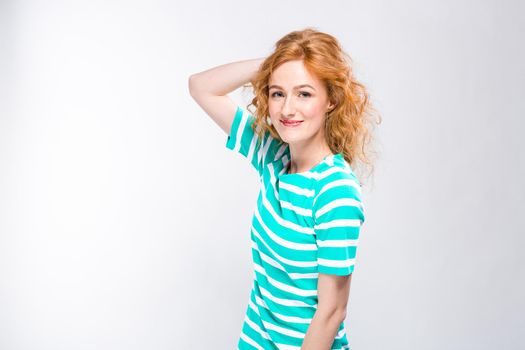 Close-up portrait of a young, beautiful woman with red curly hair in a summer dress with strips of blue in the studio on a gray background. Theme of summer vacation, tourism and summer clothes.