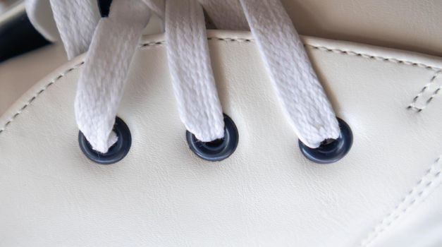 White leather sneakers lace-up shoes. White laces are tied close-up. Blurred background. Sports concept. Metal rivet for shoes as a detail or an element. Fashionable and stylish footwear
