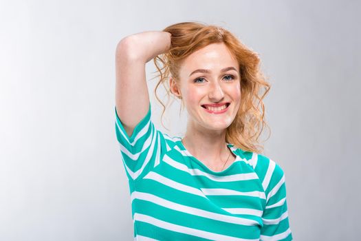 Close-up portrait of a young, beautiful woman with red curly hair in a summer dress with strips of blue in the studio on a gray background. Theme of summer vacation, tourism and summer clothes.