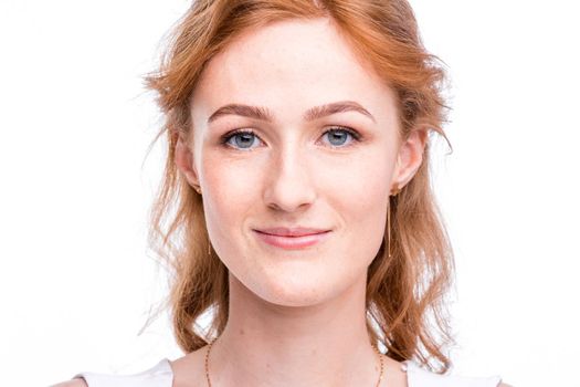 Portrait of a beautiful young woman of European, Caucasian nationality with long red hair and freckles on her face posing on a white background in the studio. Close-up student girl in a white blouse.