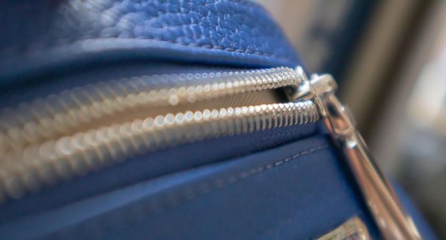 Natural or artificial leather texture. Fragment of a blue bag with a zipper and stitching. Zipper or clasp bag design element. Bovine skin texture with snake. Macro photo, selective focus