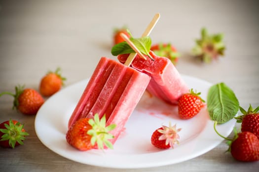 homemade strawberry ice cream on a stick made from fresh strawberries in a plate on a wooden table