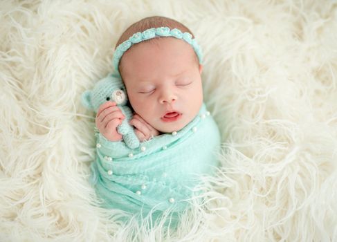 Sleeping adorable newborn baby child, in blue colored blanket and with floral headband