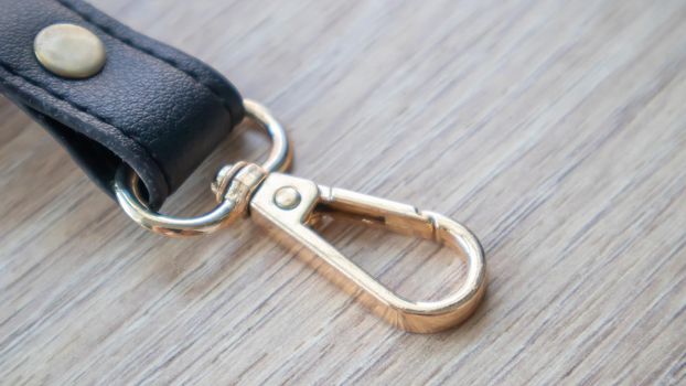 Swivel carabiner fastener with leather black bag strap on a wooden background. Metal carabiner with swivel clip or hook. Small gold fittings close-up in selective focus