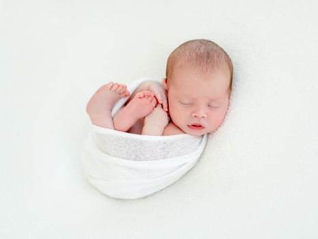 Newborn beatiful cute baby sleeping curled up in white blanket on white bed background