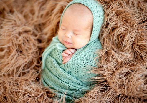 Smiling asleep newborn covered with knitted blanket