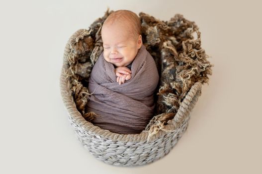 Funny newborn in basket wrapped with blanket