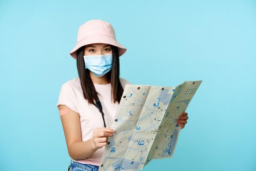Vaccinated korean woman in medical face mask, holding tourist map, visiting sightseeing on journey.