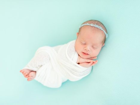 Sleeping adorable newborn baby child, in blue colored blanket and with floral headband