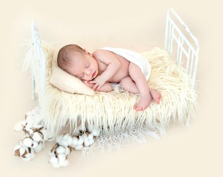 Newborn beatiful baby lying on miniature child bed, covered in fur