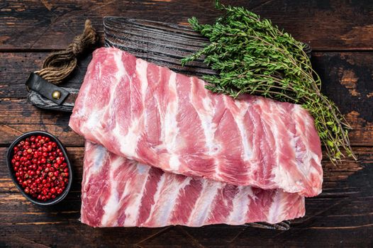 Rack of Fresh Raw pork spare ribs on butcher board. Dark wooden background. Top view.