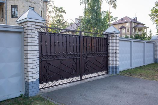 Modern private brown wrought iron large gate of the house. Home design and decoration ideas. Iron door for yard fencing. Facade of a house on a city street
