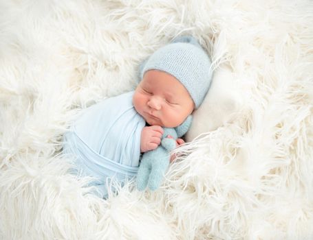 Sleeping newborn in knitted hat hugging toy