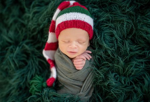 Cute newborn in knitted christmas hat lying on dark green plaid