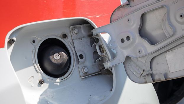 Fuel cap of a white sports car. Close the gas tank cap. The fuel tank is open. The fuel filler door is open and the fuel filler flap is closed. The exterior of the car with the filler door open