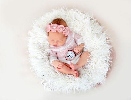 Lovely newborn baby holding clock in little hand