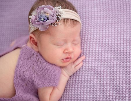 Adorable newborn in knitted purple suit and floral diadem