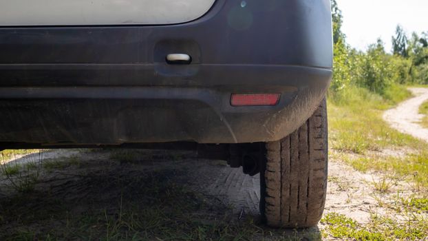 Passenger side of a white modern car on a dirt road, rear view of the bumper and wheel. Very low plan