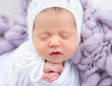 Charming newborn in white knitted hat sleeping close up