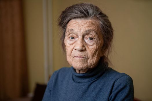 Elderly Caucasian senior grandmother ninety years old looks attentively and smiles, feels happy, large portrait, face with deep wrinkles, gray hair. Theme pensioners, old people and long-lived woman.