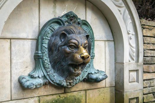 Lion head fountain on the wall. Vintage brick wall texture with lion shaped stucco. The molded face of a lion is sprayed with water. Bas-relief lion fountain
