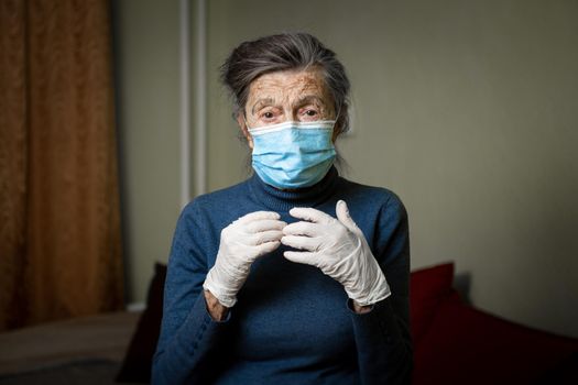 Portrait elderly woman took security measures, wearing gloves and medical mask, ahead of visit by social welfare workers during coronavirus quarantine. Lockdown and loneliness, need for care.