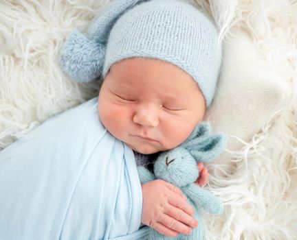 Sleeping newborn in knitted hat hugging toy
