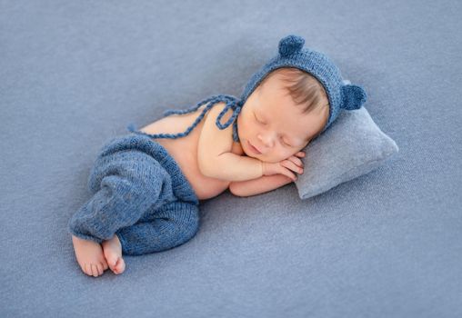 Charming newborn in cute hat sleeping on tiny pillow